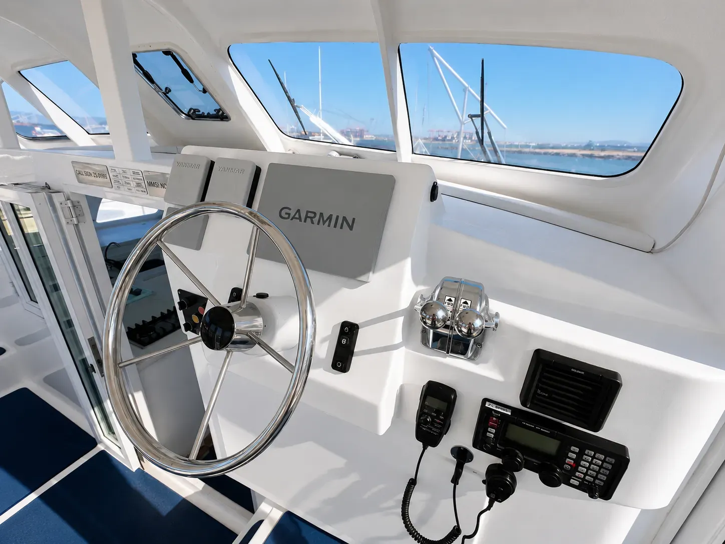 Vaquita's helm station with a stainless-steel wheel, Garmin chartplotter, engine throttles, and VHF radio.