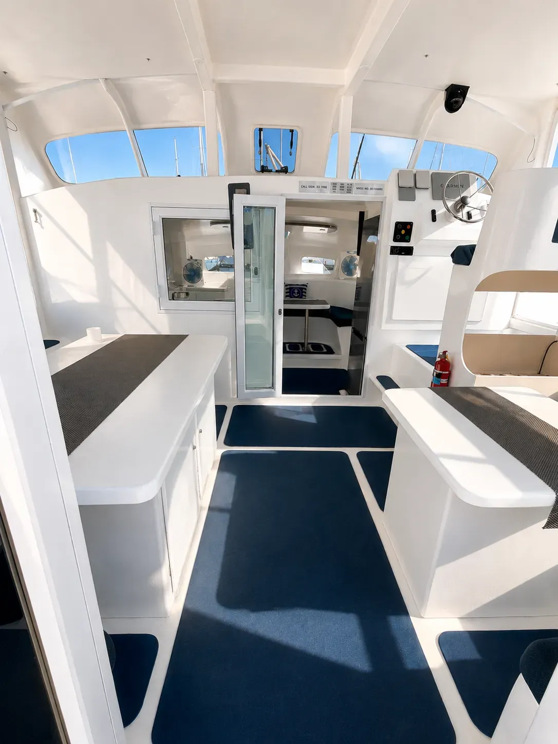 Wheelhouse aboard Vaquita looking aft through a sliding door, with bench seating to port and starboard and the helm station to one side.
