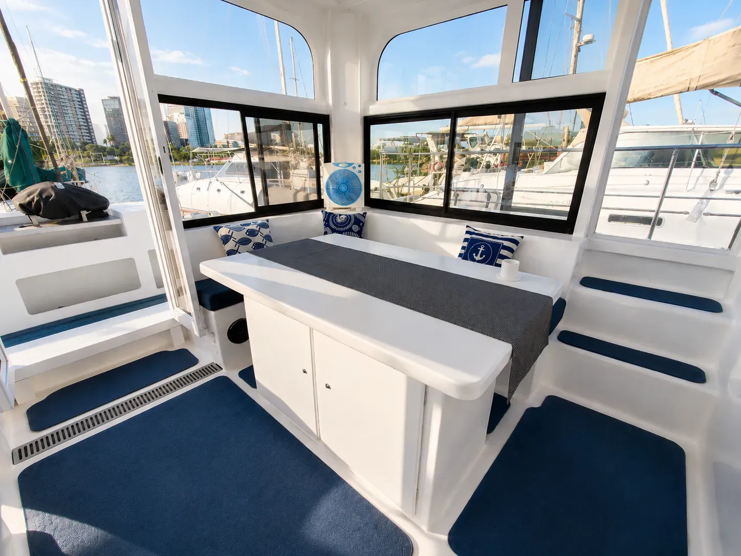 Work table and L-shaped bench seating aboard Vaquita beneath wraparound windows, set up for meals or mission planning.