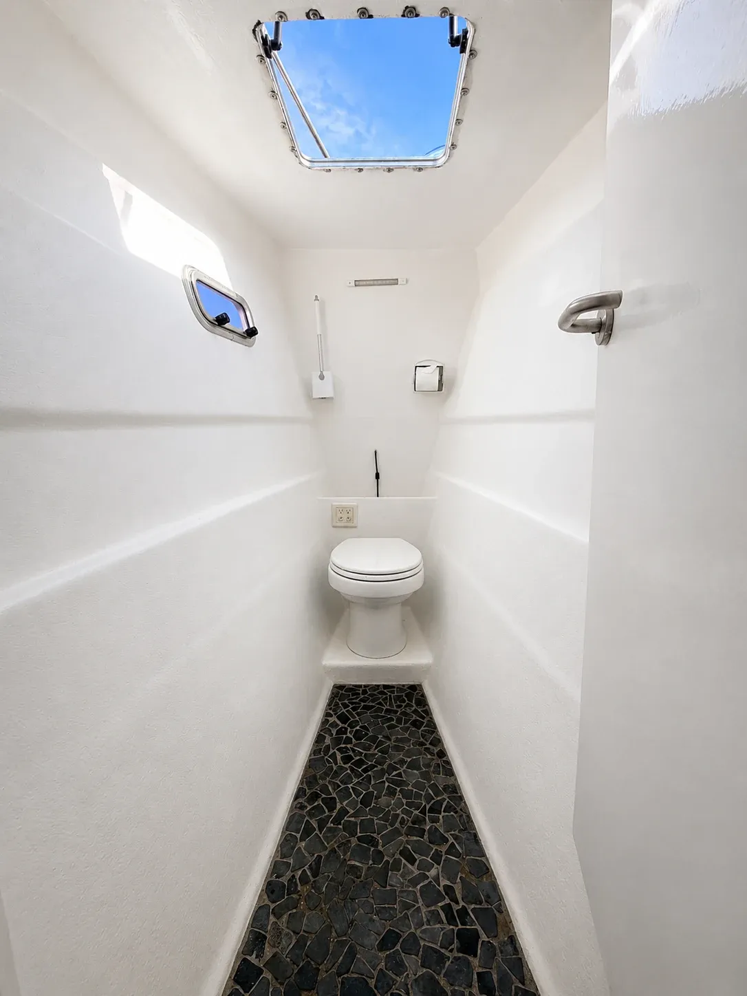 Private ensuite head aboard Vaquita with an electric toilet, porthole, and overhead hatch.