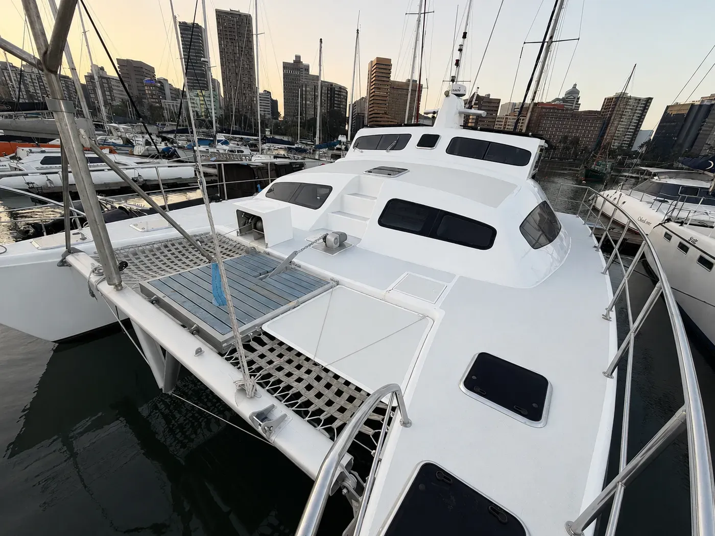 Vaquita's bow seen from forward, showing the foredeck hatches, trampoline nets, and the wheelhouse against the Durban skyline.