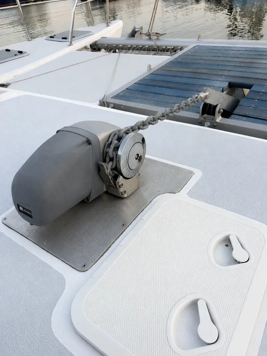 Vaquita's foredeck windlass with galvanised anchor chain running over the gypsy beside a deck hatch.