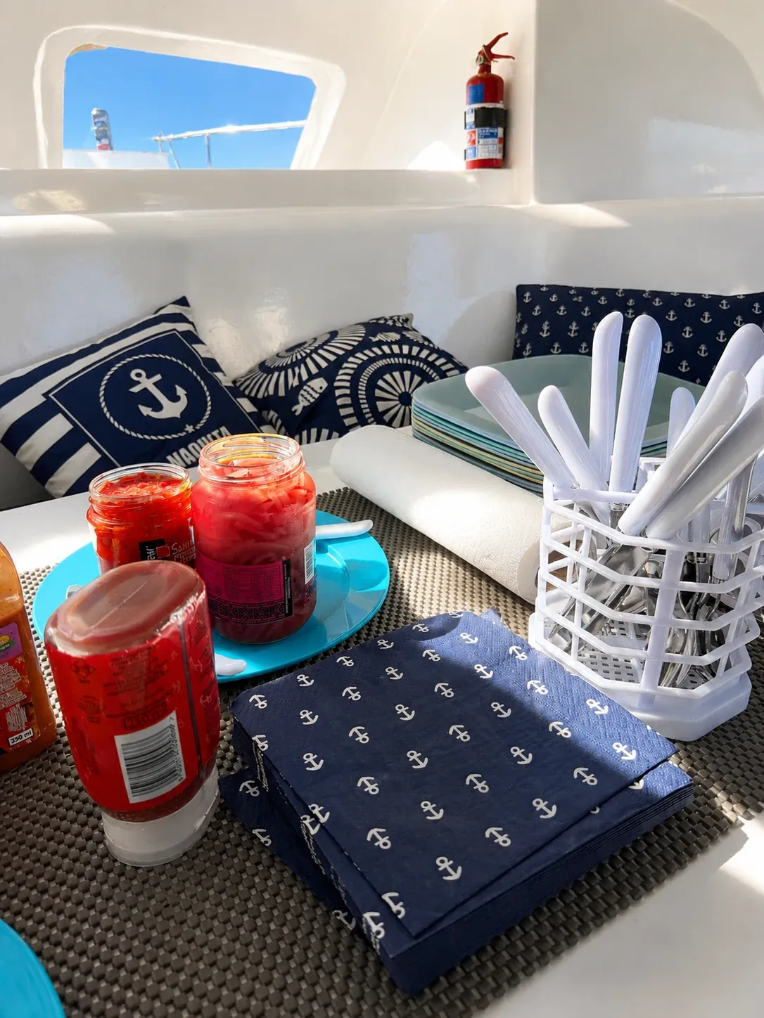 Galley seating set with provisions, stacked plates, and nautical napkins ready for a meal at sea.