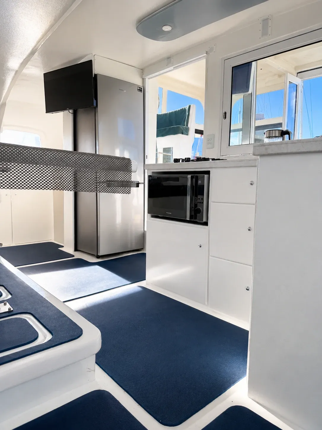 Galley aboard Vaquita with a double-door stainless fridge/freezer, microwave, and a wall-mounted TV monitor.
