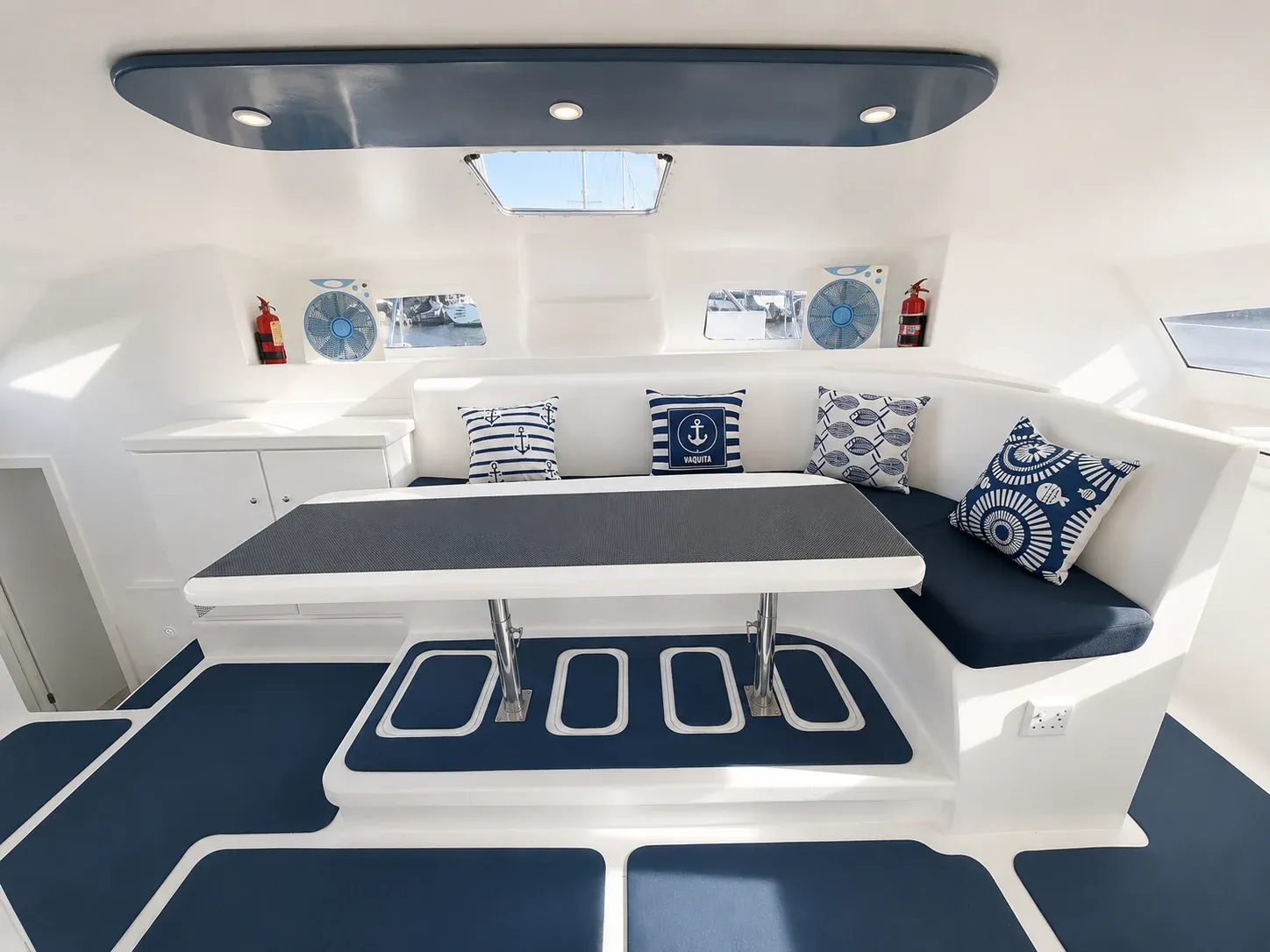 Vaquita's main saloon: L-shaped seating with nautical cushions around a central dining table.