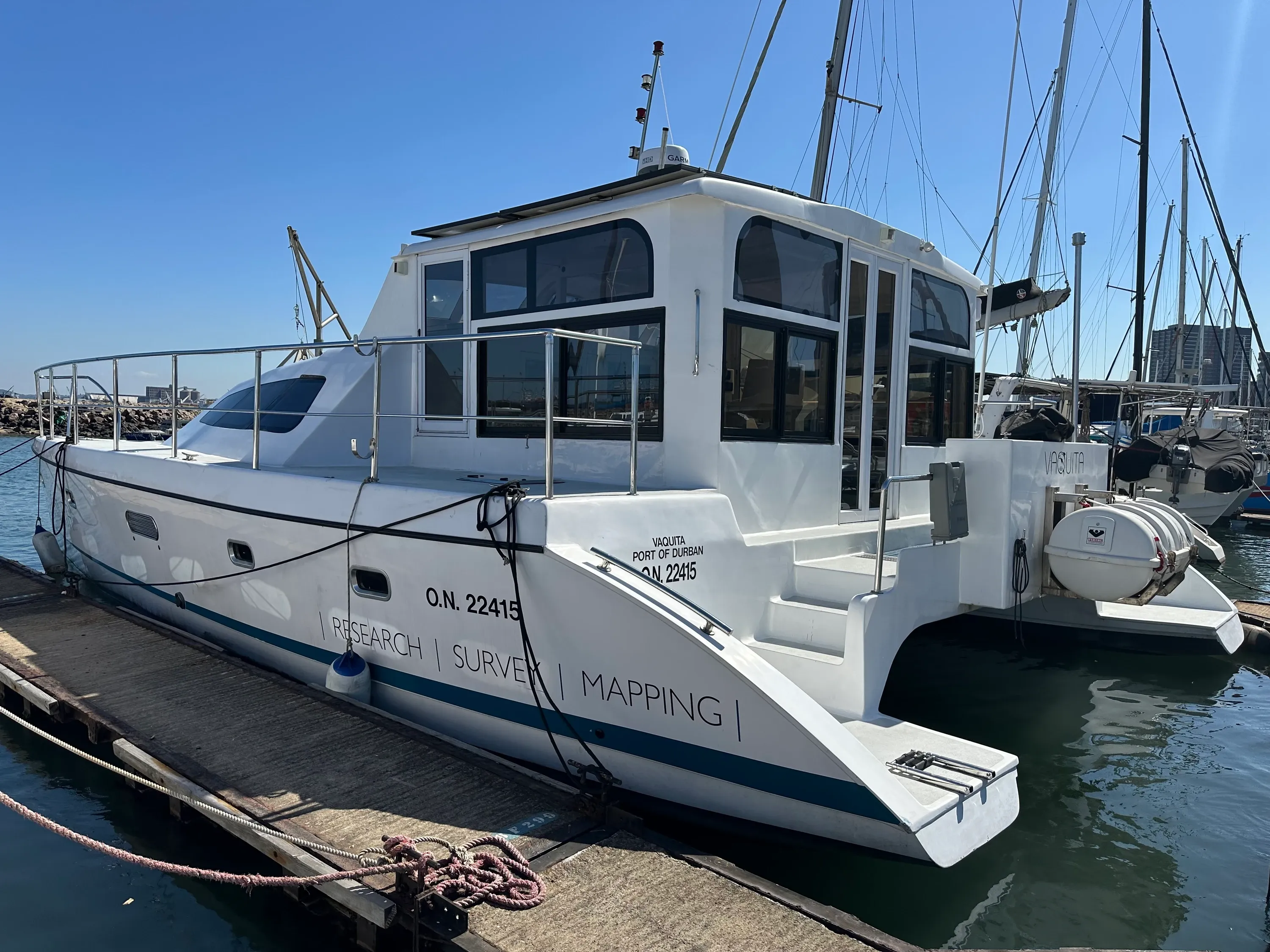 Vaquita's full port side at her Durban berth, clean and rigged ready for a day at sea, the hull marked 'RESEARCH | SURVEY | MAPPING' and 'O.N. 22415' with the marina behind.