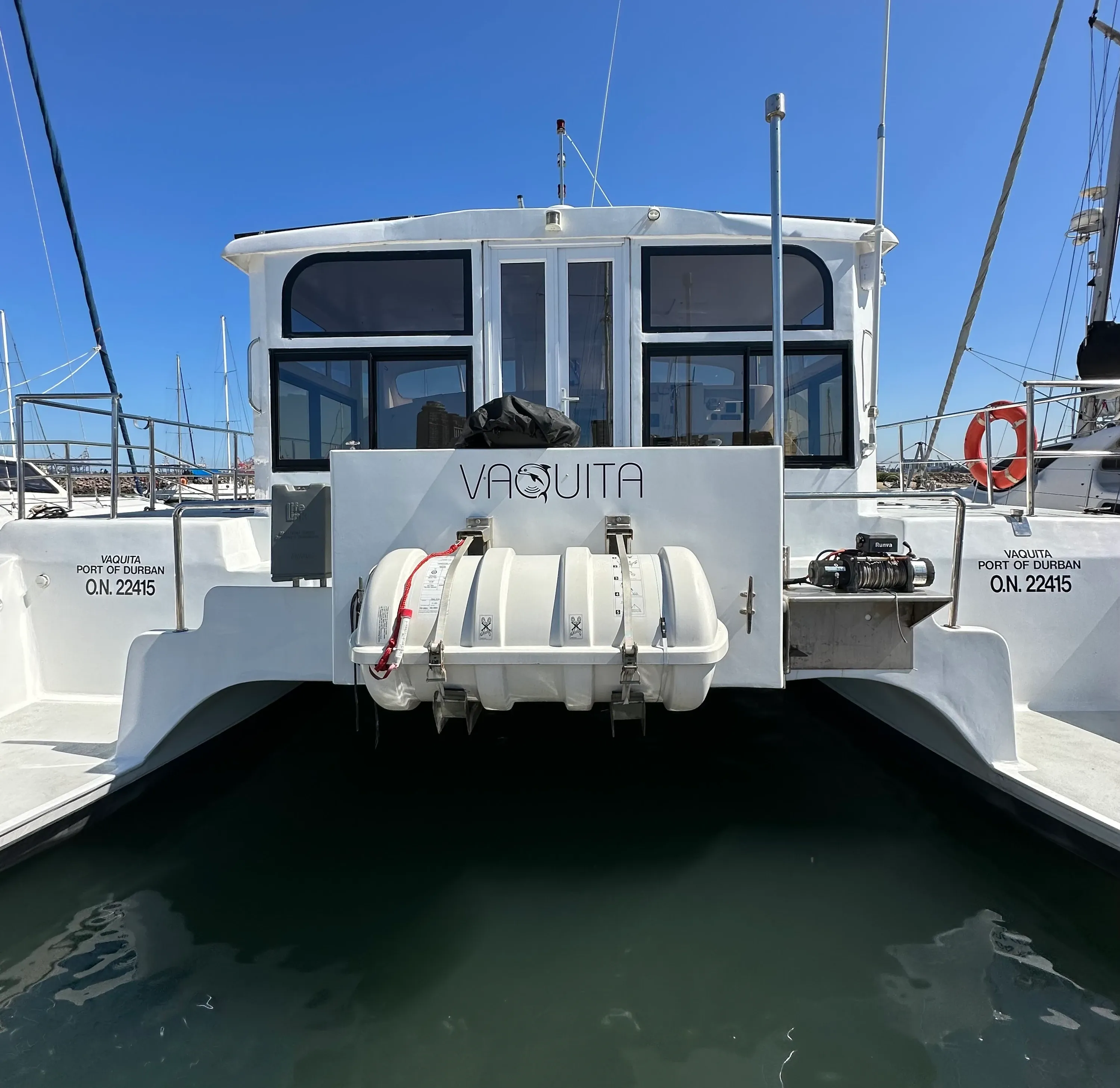 Vaquita seen stern-on at her berth, both transoms marked 'VAQUITA, Port of Durban, O.N. 22415', with the life raft canister and winch between the hulls.
