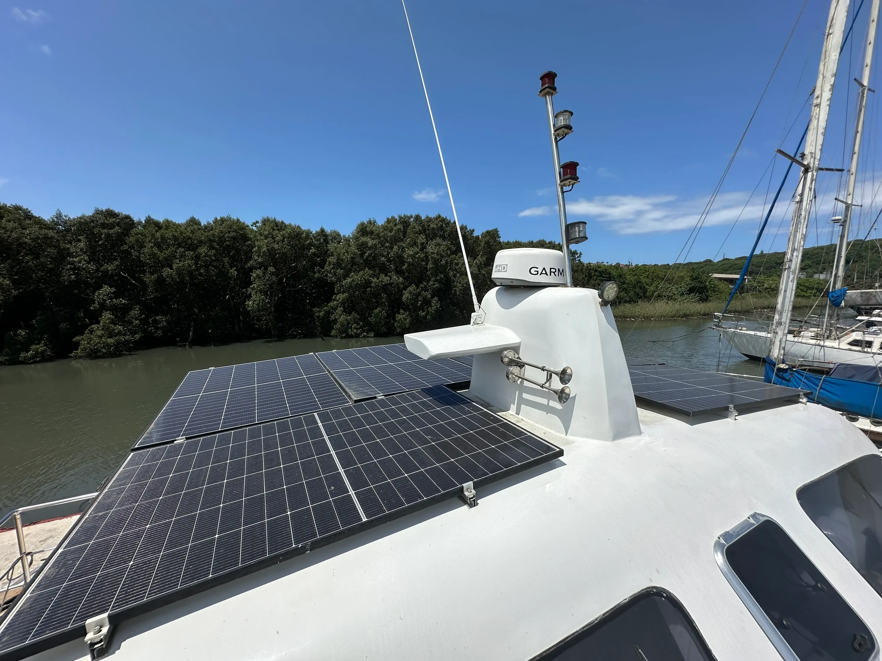 Vaquita's cabin top with its bank of solar panels and the mast carrying the Garmin radar dome and antennae, mangroves along the river behind.