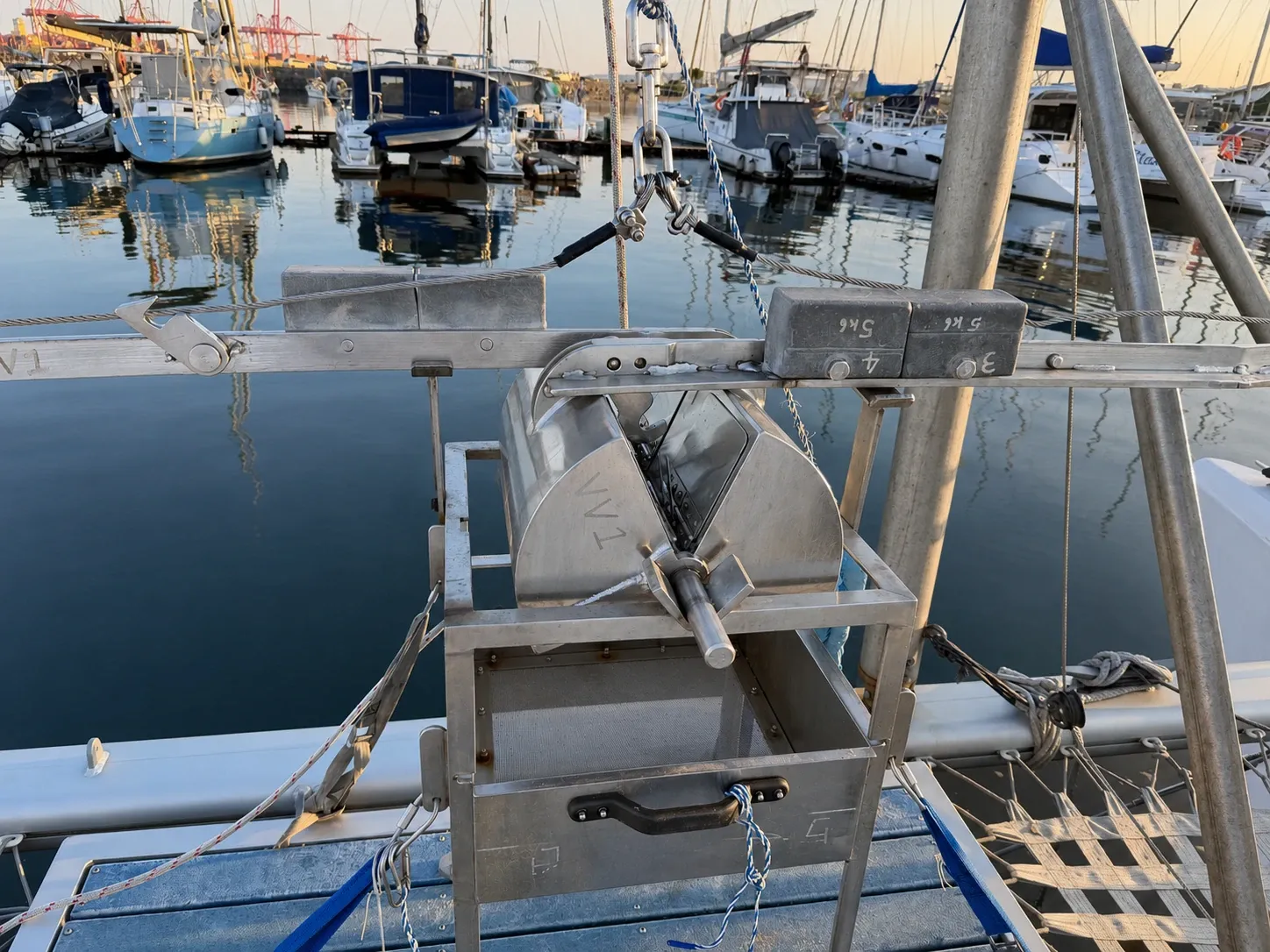 Close view of the stainless grab sampler and A-frame workstation rigged on Vaquita's bow at dusk, the marina water behind.