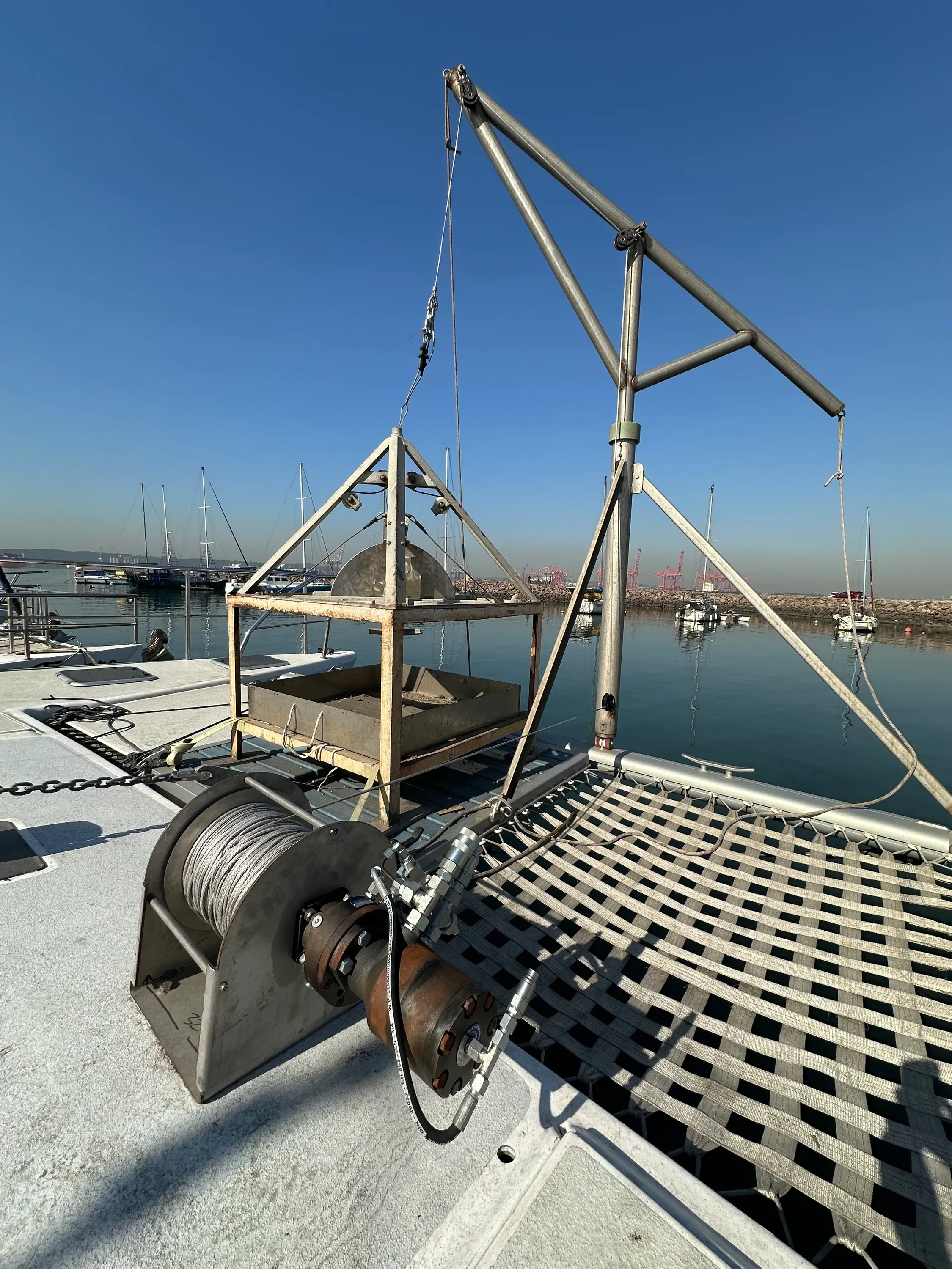 Vaquita's foredeck rigged for survey work: A-frame davit, sampler cradle, and the steel-cable winch drum on the bow under a clear sky.