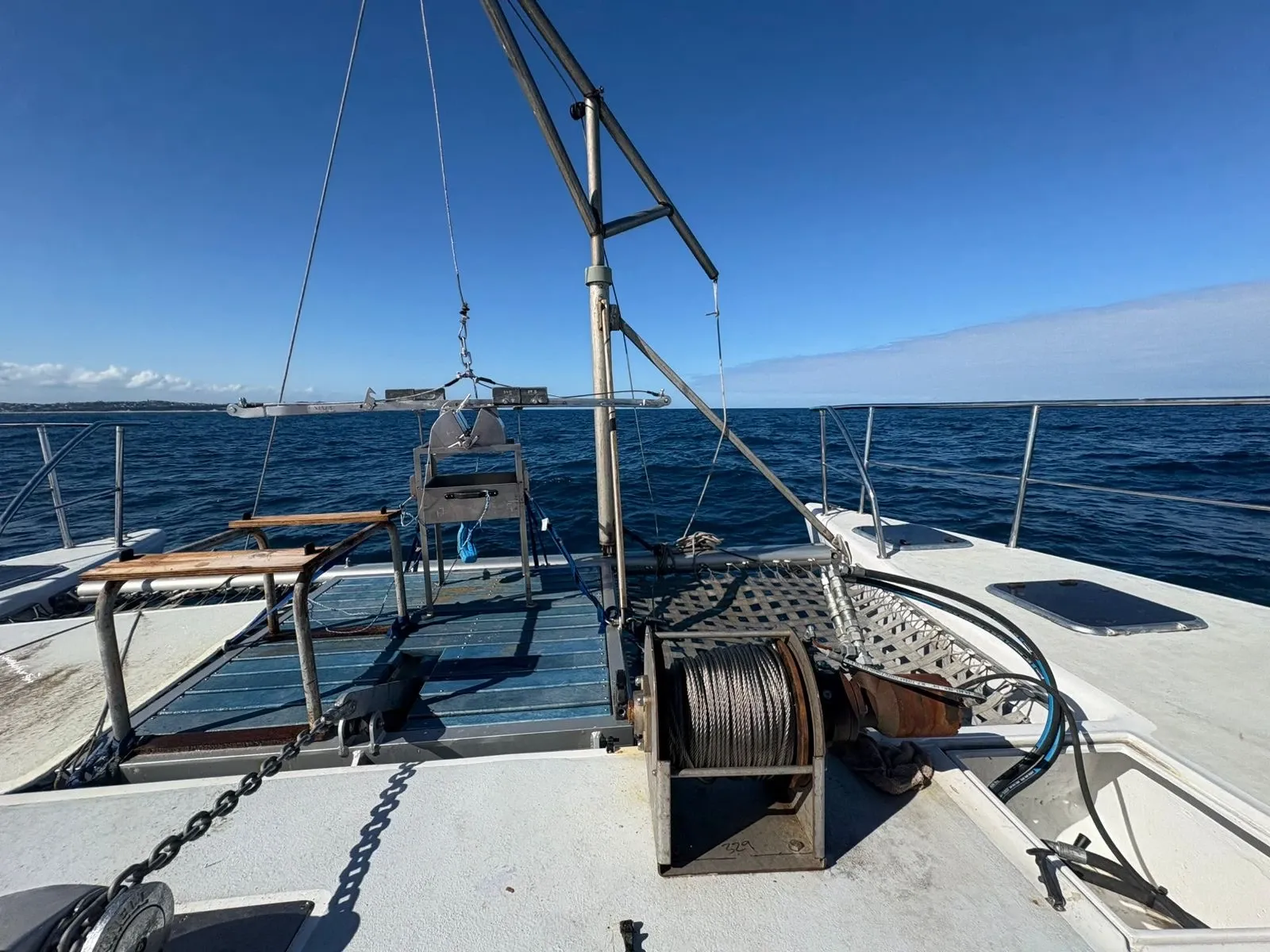 Looking forward along Vaquita's foredeck rigged for survey, the A-frame davit, winch drum, and deck workstation with open sea and coastline ahead.